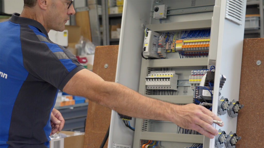 Mitarbeiter der Elektro Kaufmann GmbH, der vor einem offenen Schaltschrank mit diversen elektronischen Bauteilen arbeitet.